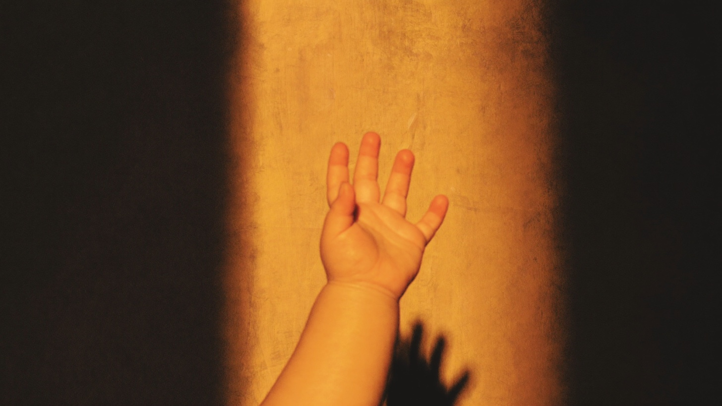 An infant's open hand reaching toward a band of warm light