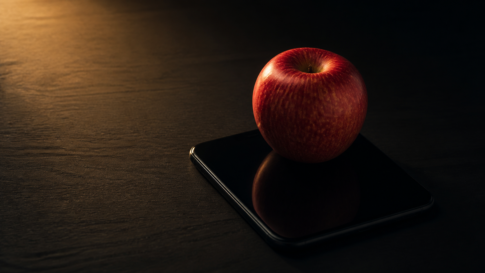 A red apple resting on the black glass of a phone in warm low light